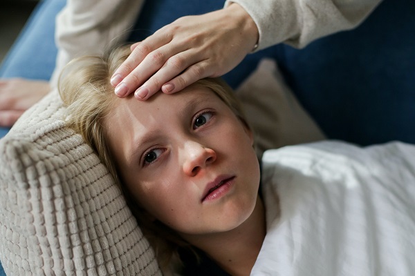 baietel care nu se simte bine si sta in pat in timp ce mama lui il atinge pe frunte sa vada daca are febra