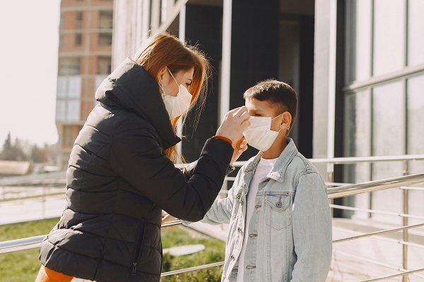 femeie cu masca de protectie care îi fixeaza masca de protectie pe fata unui baietel