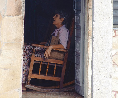 femeie matura care sta pe un fotoliu din lemn care se leagana in casa ei