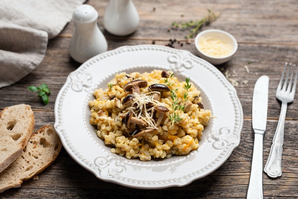 risotto cu ciuperci, decorat cu verdeata si cu parmezan ras, intr-o farfurie alba