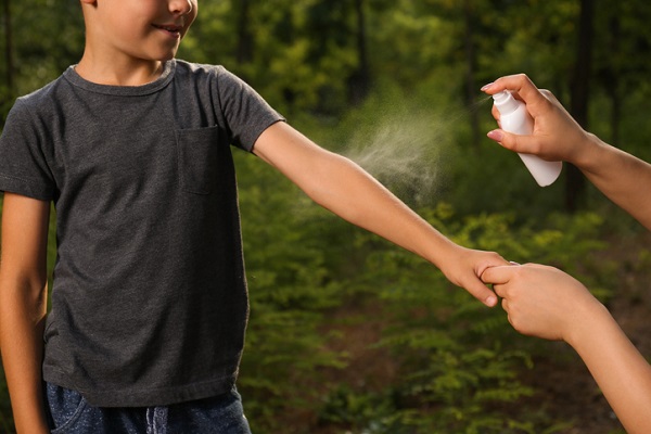 femeie care pulverizeaza spray contra insectelor pe bratul unui baietel