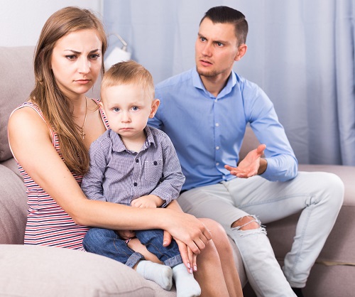 mama suparata, tinandu-si baietelul in brate, in timp ce partenerul ei sta langa ea si este furios