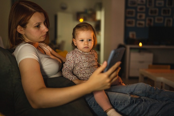 mama tanara, trista, tinandu-si seara fetita in brate si uitandu-se pe telefon