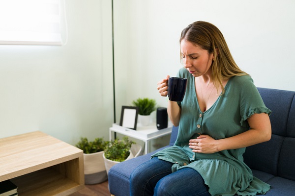 femeie care sta pe canapea, care se confrunta cu disconfort abdominal si bea un ceai