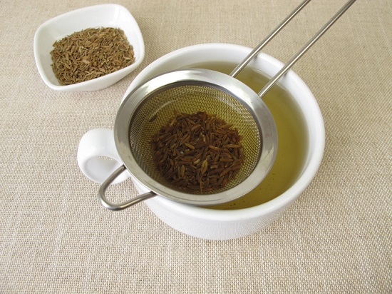 seminte de chimen intr-un castronel alb, ceai de chimen pus in cana si strecuratoare pentru ceai
