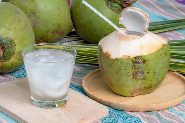 pahar cu apa de cocos langa o nuca de cocos verde, sectionata in partea superioara