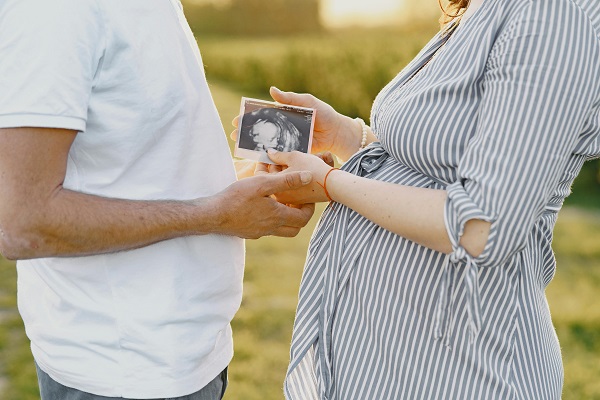 femeie insarcinata si partenerul ei tinandu-se de mana, viitoarea mama tinand in mana si o imagine de la o ecografie fetala