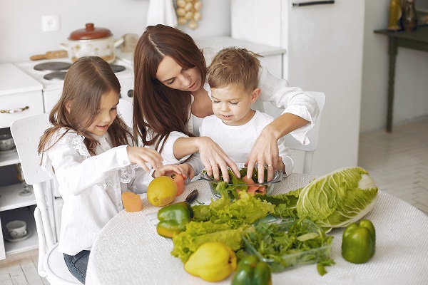 mama si cei doi copii ai ei in bucatarie, incercand sa pregateasca o salata cu legume cu frunze verzi