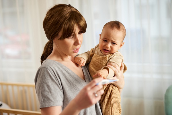 mama care isi tine bebelusul in brate si se uita ingrijorata la termometru