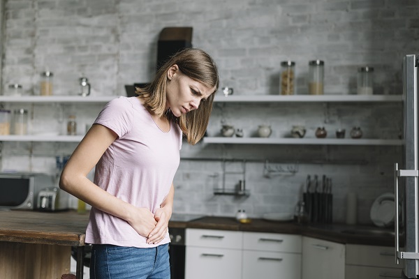 femeie tanara care sta in bucatarie si se confrunta cu o durere abdominala