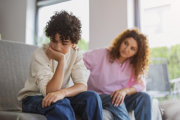 mama care sta pe canapea langa fiul ei adolescent si incearca sa il consoleze