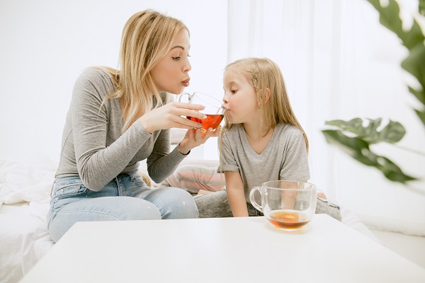 mama care îi da fetitei sale ceai dintr-o cana de sticla