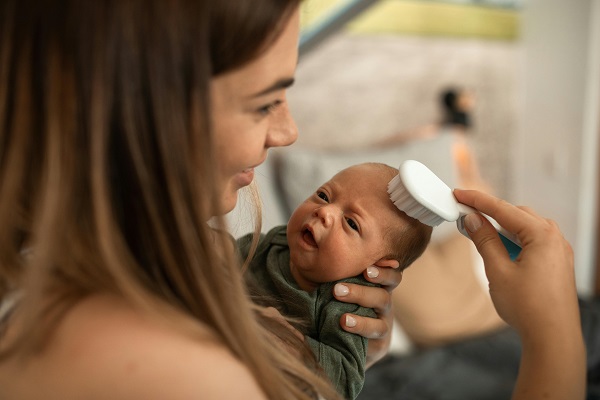 mama zambitoare care isi tine in brate nou-nascutul si incearca sa-l pieptene