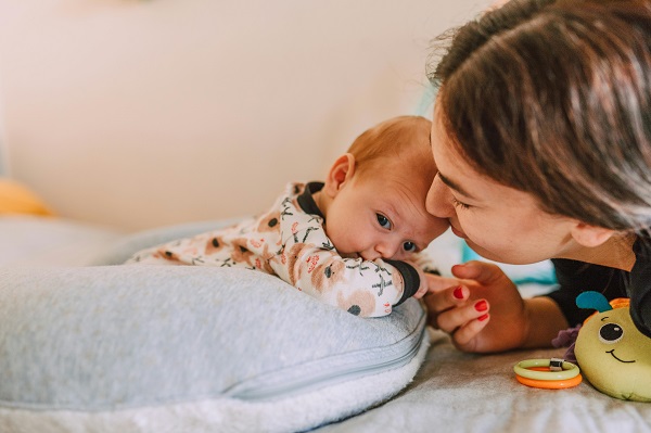 mama care sta alaturi de bebelusul ei intins pe burtica pe o perna de alaptare gri