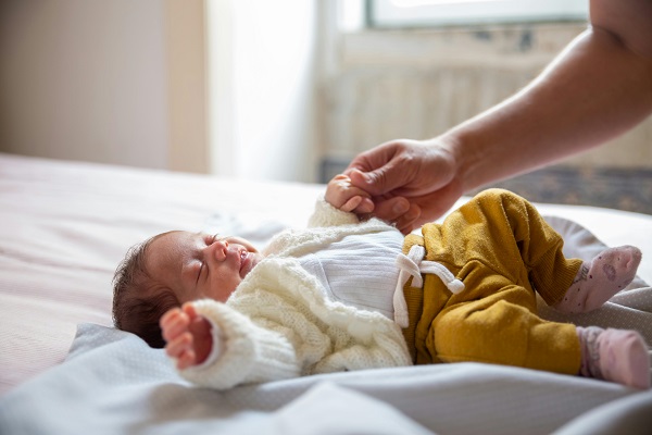 femeie care tine de mânuta un nou-nascut intins pe spate intr-un pat