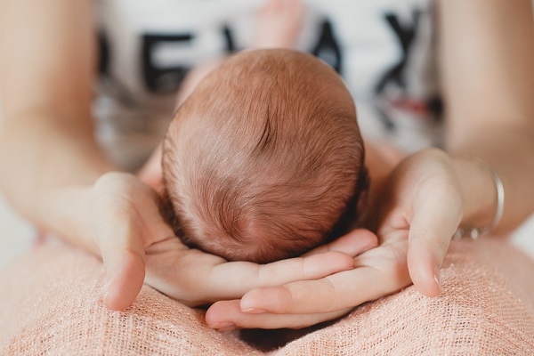 femeie care tine in palme capul unui bebelus ce sta in poala ei