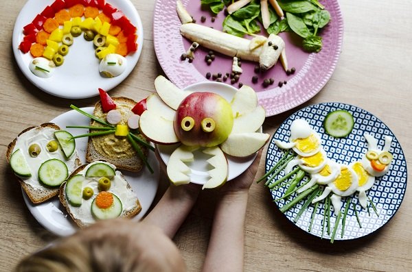 copil care sta in fata unor farfurii cu alimente sanatoase, frumos decorate si aranjate