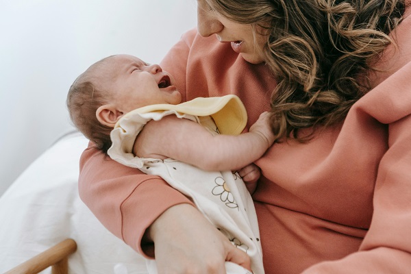 mama care isi tine in brate bebelusul si incearca sa il calmeze