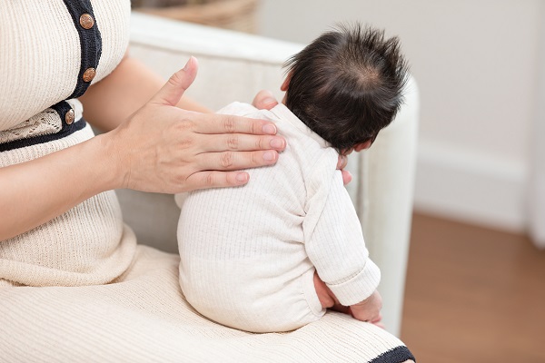 mama care isi tine bebelusul pe genunchi si il bate pe spate ca sa eructeze sau in caz de sughit