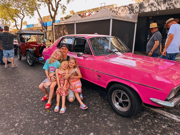 tata cu trei fete in multime langa o masina roz