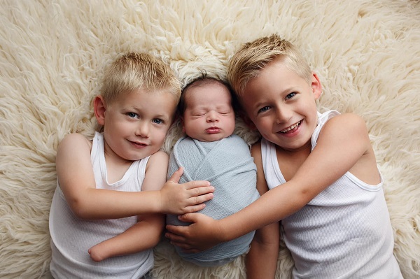 trei băieti frati intr-un pat in mijloc un bebelus si unul din băieți nu are o mână