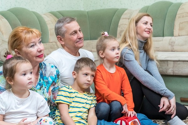 familie numeroasa adulti si copii privesc la tv
