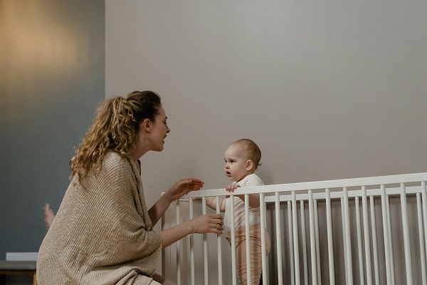 mama vorbeste cu bebelusul care este in patut de lemn cu gratii