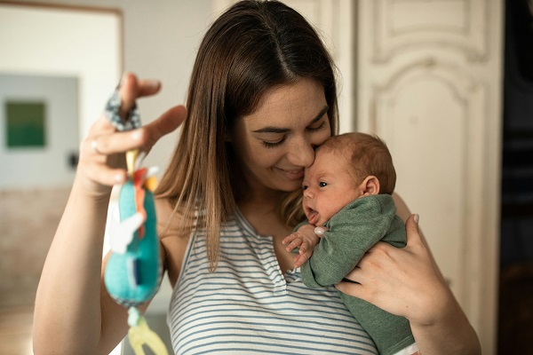 femeie tine un bebe in brate ii arata o jucarie