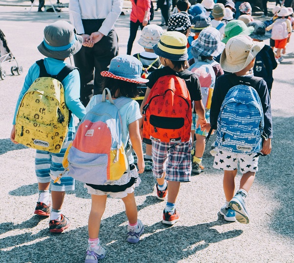 grup de copii mici cu ghiozdane in spate merg pe strada