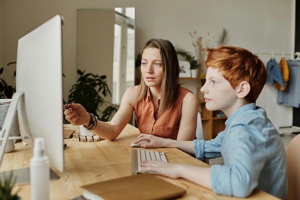 mama isi ajuta copilul la teme pe laptop pe un birou