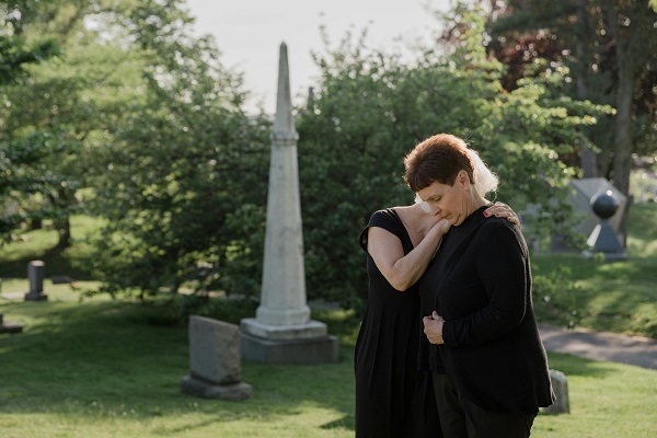 doua femei in negru intr-un cimitir se imbratiseaza si plang