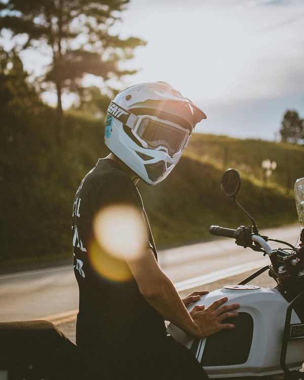 baiat pe motocicleta isi pune o casca pe cao