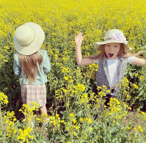 doua fetite cu palarii in cap se joaca in lanul cu rapita