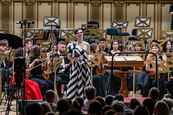 fiica ozanei barabancea in rochie lunga alb cu negru prezinta pe o scena cu orchestra in spate